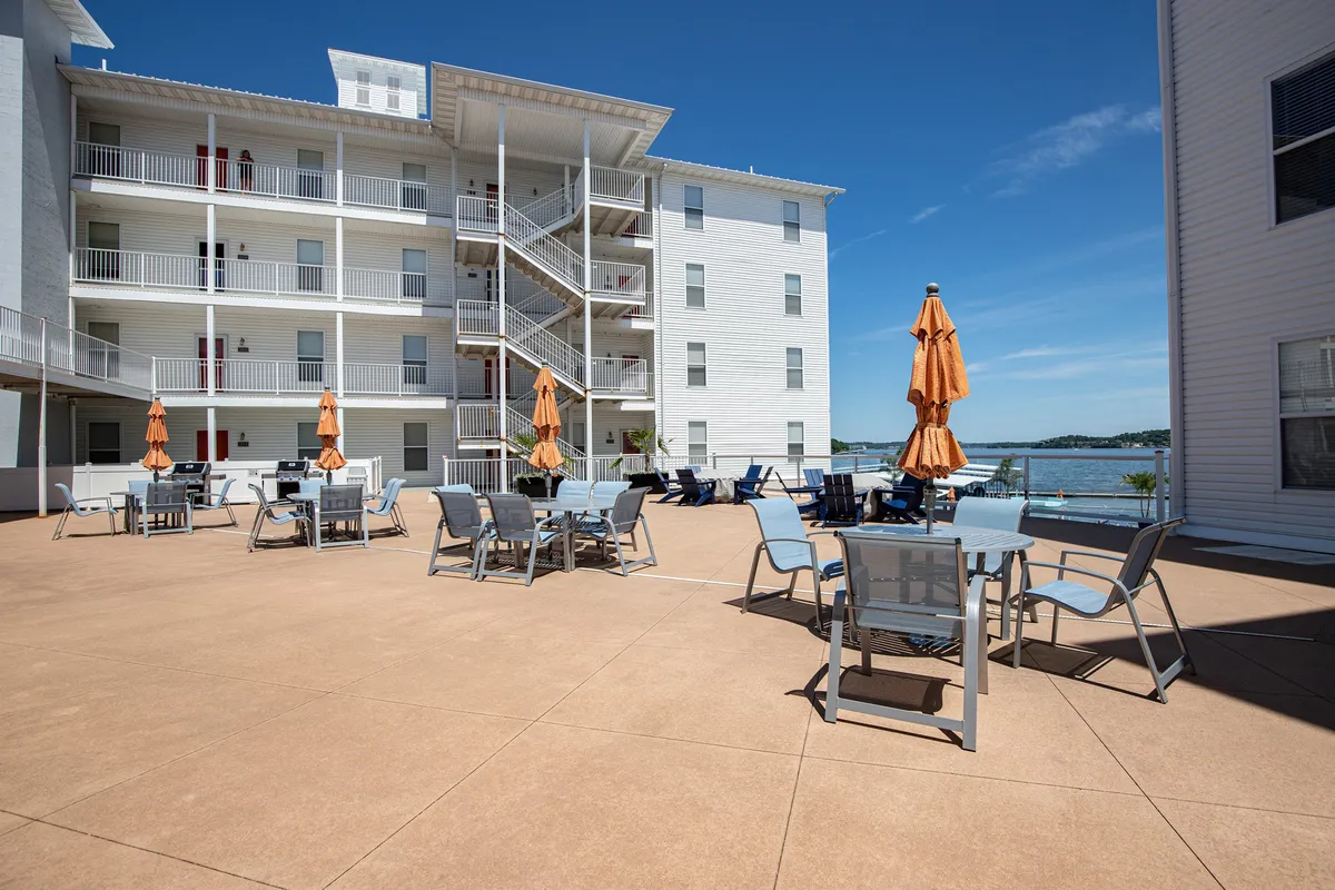 An inviting outdoor seating area beneath orange umbrellas, set against a stunning water backdrop. The setup encourages socializing and relaxation, with ample space for gatherings and unobstructed views for watching the sunset or enjoying meals outdoors.