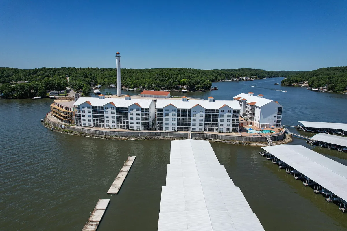 A broad view of the waterfront property, showing the modern dock area, lush greenery, and serene lake. The scene includes the dock, an essential amenity for boating and fishing, and conveys the tranquil, exclusive vibe of the community.