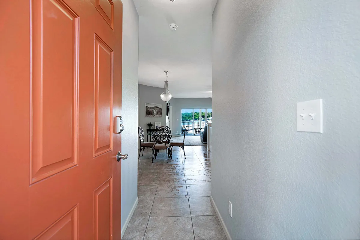 This inviting interior shot captures the orange front door opening into a bright dining area, accented by tile flooring and natural light streaming in from the windows. The setup evokes a welcoming atmosphere ideal for family arrivals and group meals, with direct sightlines toward the patio area outside.
