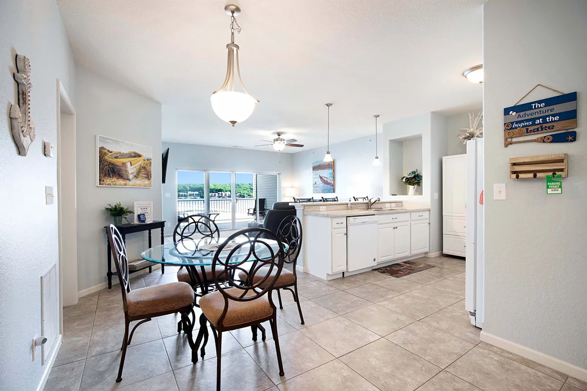 A spacious dining table with a glass top is the centerpiece of this room, which features an open kitchen and large windows revealing views of the outdoors. The area is filled with natural light, perfect for family feasts and group celebrations.