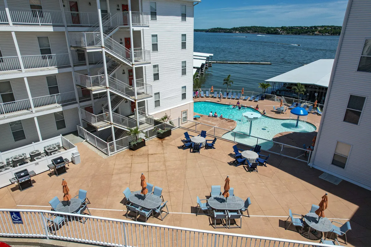 This image captures the resort's inviting swimming pool framed by comfortable outdoor seating areas, all with a picturesque view of the adjacent lake and the property's architecture in the background. Children are seen playing in the water while adults relax poolside, enjoying the blend of fun and relaxation.