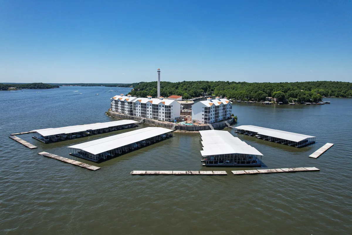 A sweeping view of the waterfront property featuring a marina, a lighthouse, and lush greenery. Guests are seen boating, fishing from the dock, and enjoying picnics by the water, capturing the variety of outdoor activities available to families.