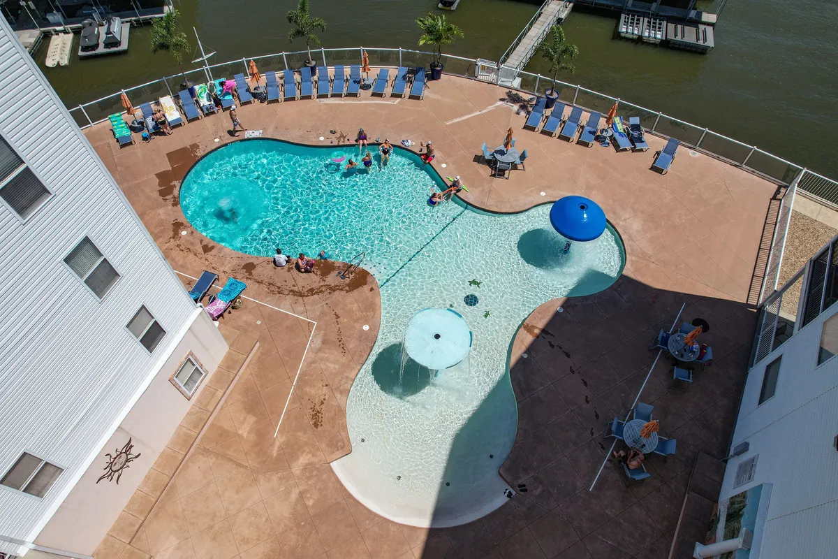 A lively pool area with sun loungers and sparkling water features, bordered by lush greenery. The scene conveys a vibrant resort-like atmosphere and emphasizes outdoor recreation and relaxation steps from the water.