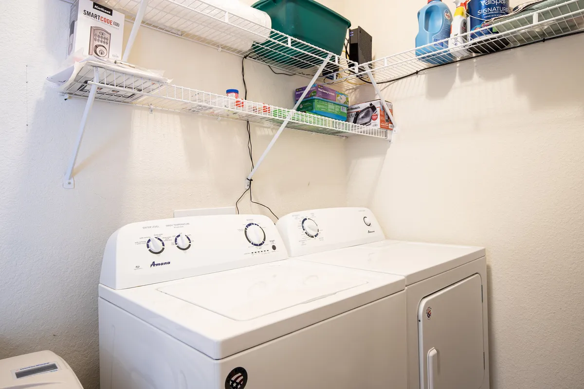 A practical laundry area featuring a washing machine, dryer, and organized shelving for cleaning supplies and linens.